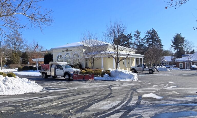 Snow-covered parking lot at a bank with plow truck.