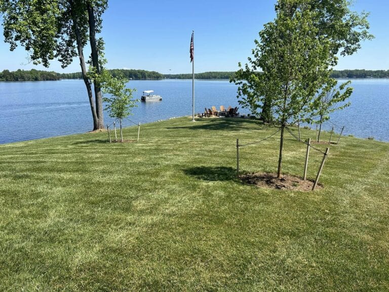 Peaceful lakeside lawn with docked boat and chairs.