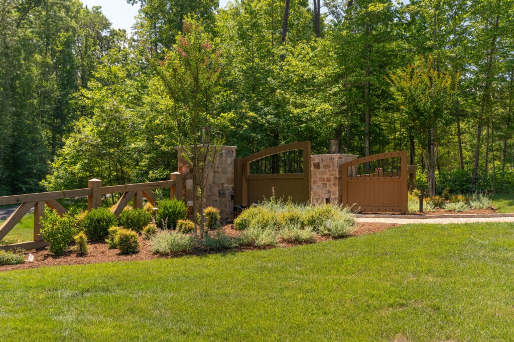Wooden driveway gate with stone pillars and landscaping